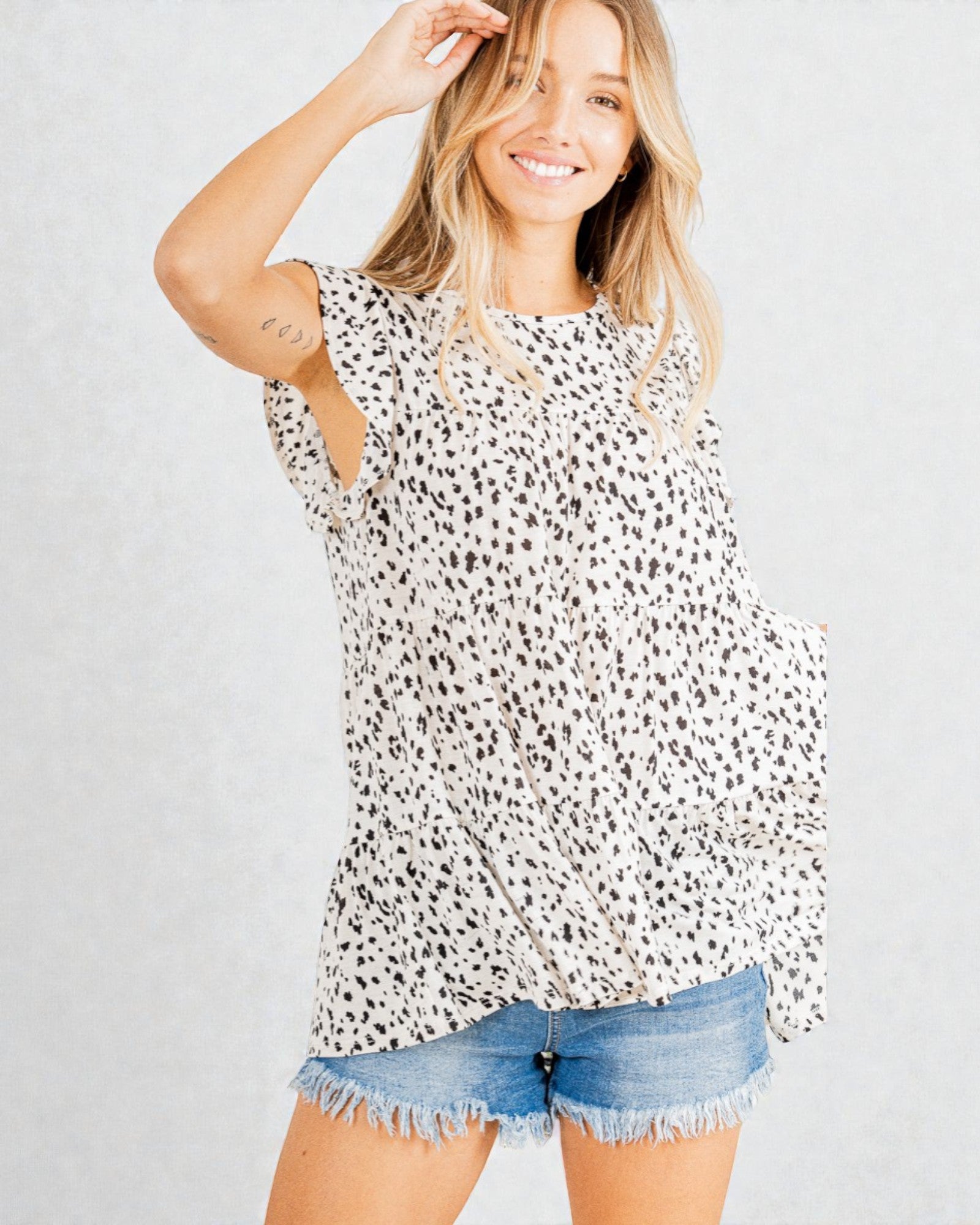 Woman wearing a black and white patterned top with denim shorts on a light gray background