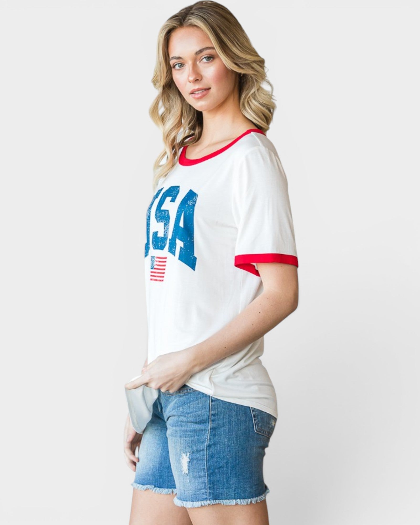 Woman wearing a white t-shirt with 'USA' print and denim shorts on a plain background