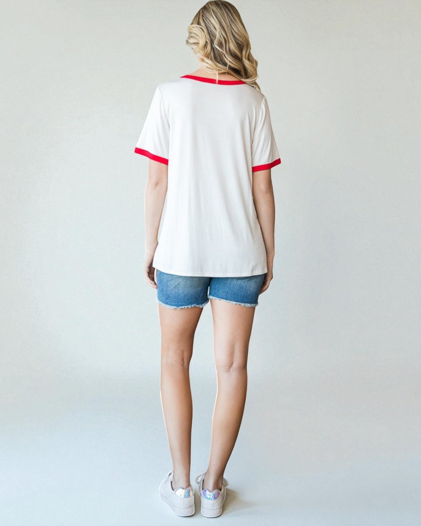 Person wearing a white t-shirt with red trim and denim shorts on a plain background