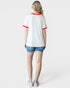Person wearing a white t-shirt with red trim and denim shorts on a plain background