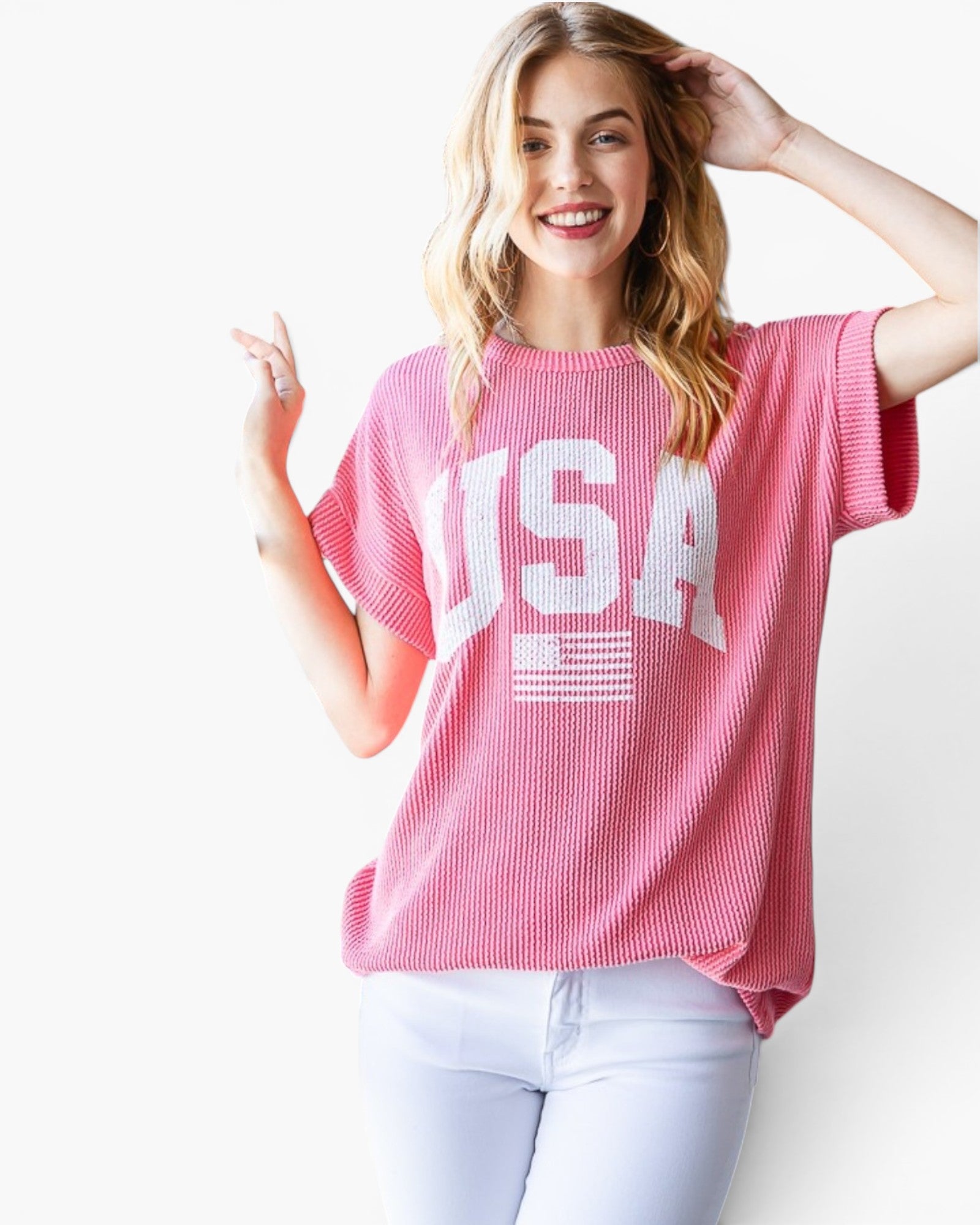 A woman wearing a pink short-sleeve ribbed t-shirt with a white 'USA' and American flag graphic on the front, paired with light blue jeans, against a plain white background.