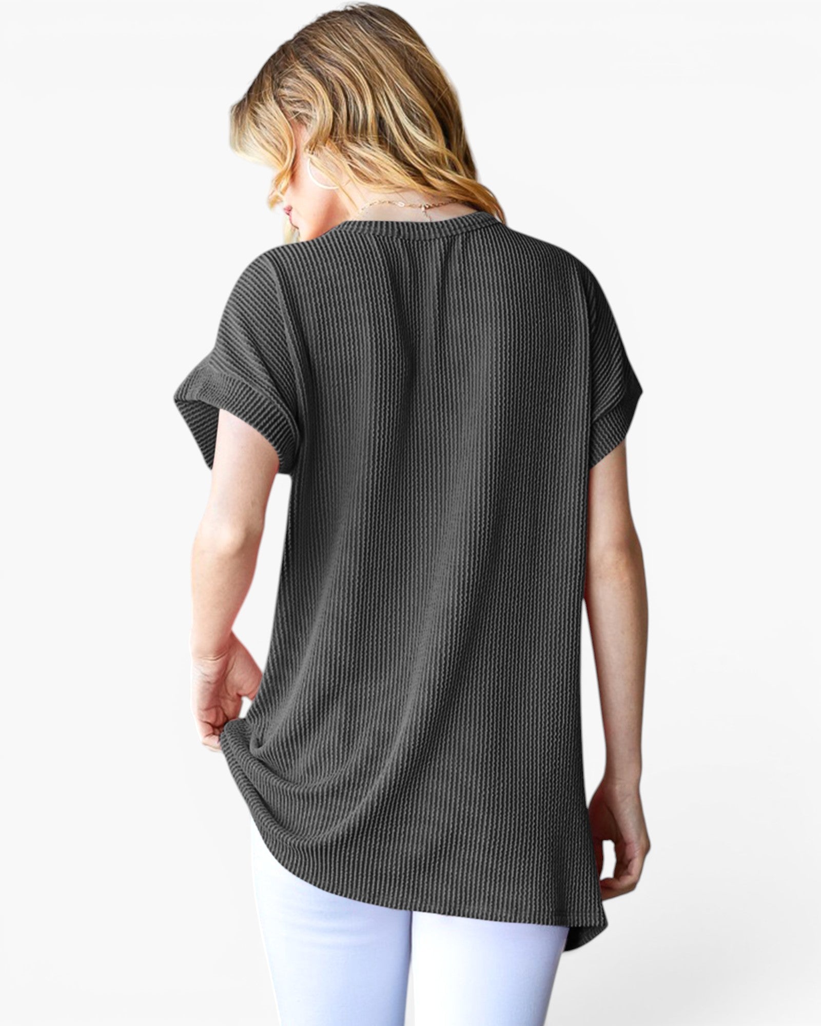 A woman shown from the back wearing a black short-sleeve ribbed tunic top and white pants against a plain white background.