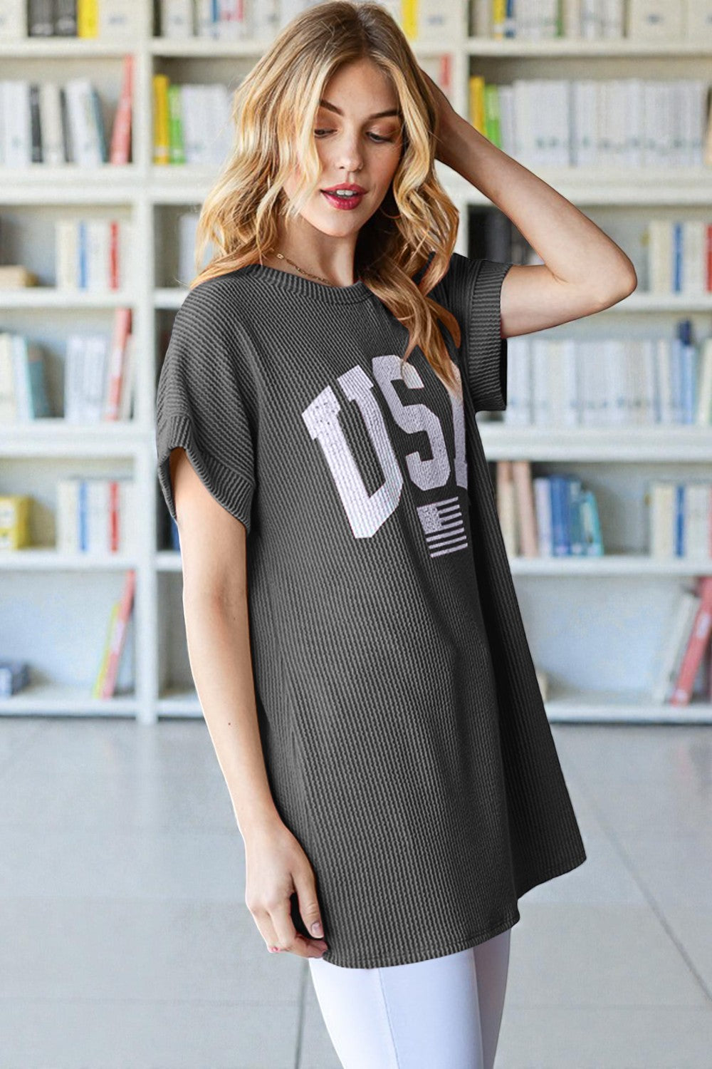 Woman wearing a dark gray t-shirt with 'USA' printed on it in a library setting.