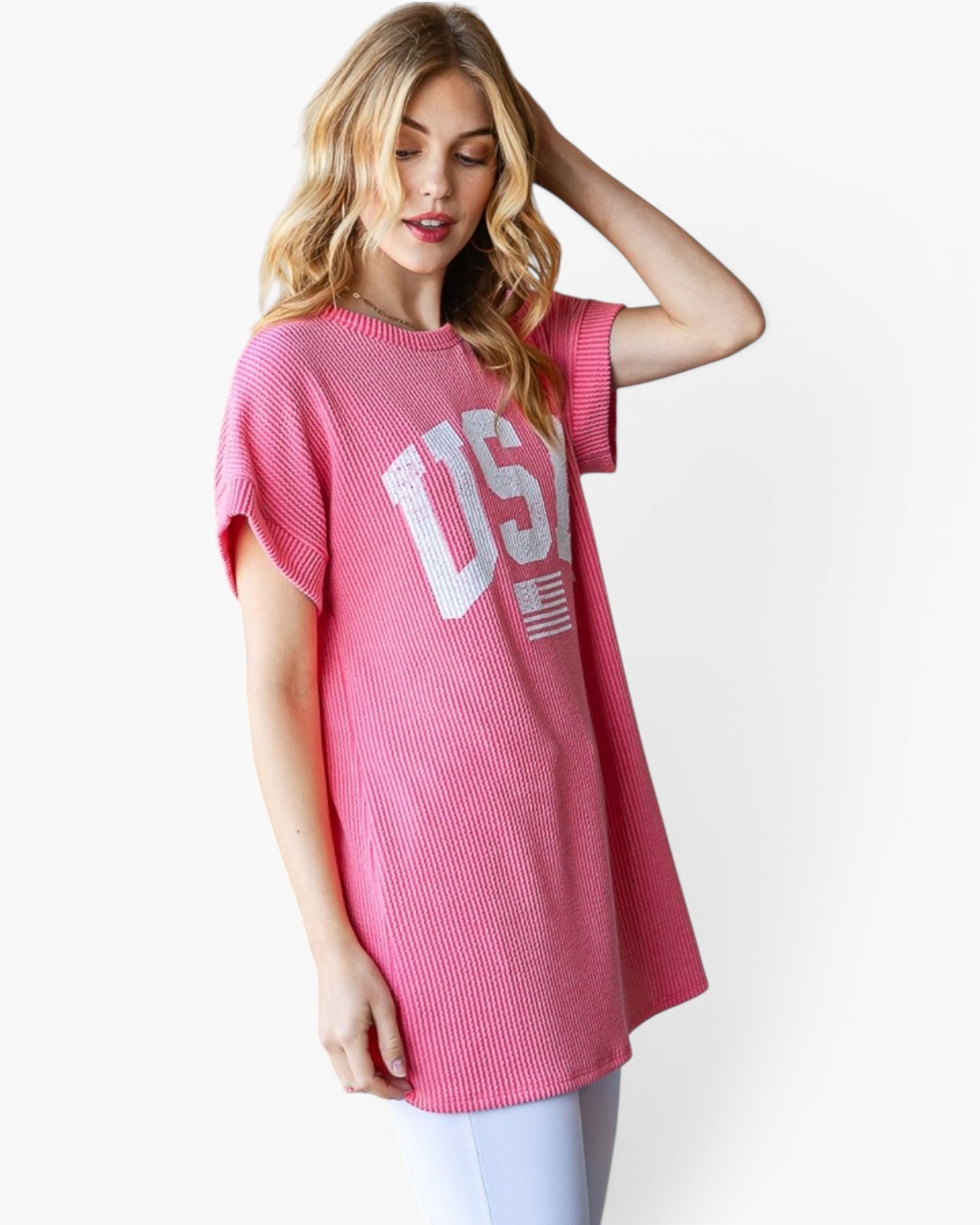 A woman wearing a pink short-sleeve ribbed knit tunic top with a white 'USA' graphic and American flag print on the front, paired with light blue leggings, against a plain white background.