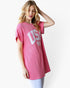 A woman wearing a pink short-sleeve ribbed knit tunic top with a white 'USA' graphic and American flag print on the front, paired with light blue leggings, against a plain white background.