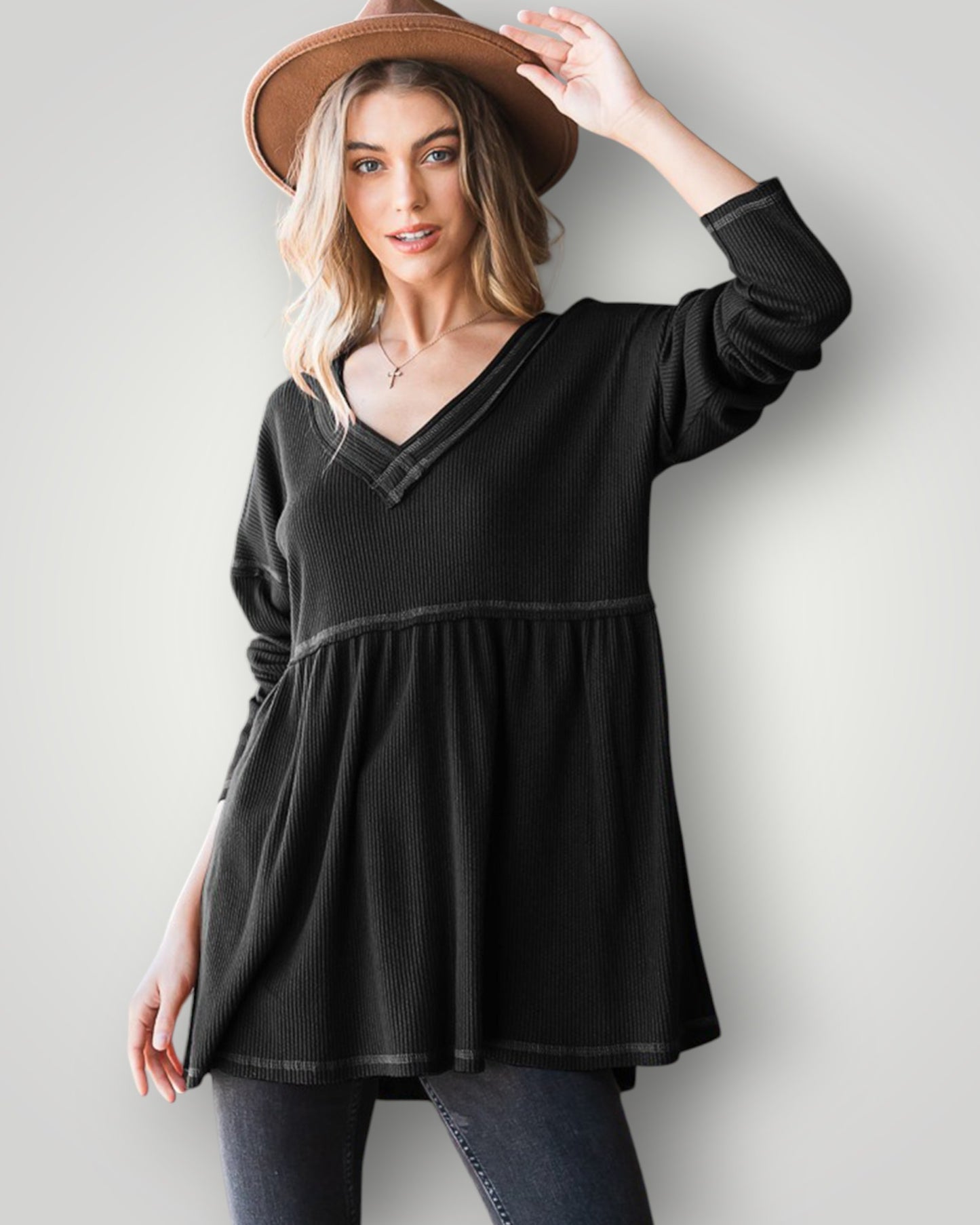 Woman wearing a black long-sleeve top and a brown hat against a plain background