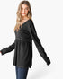 A woman modeling a black long-sleeve tunic top with a wide V-neck and gathered waist seam, paired with blue jeans against a light gray studio background.