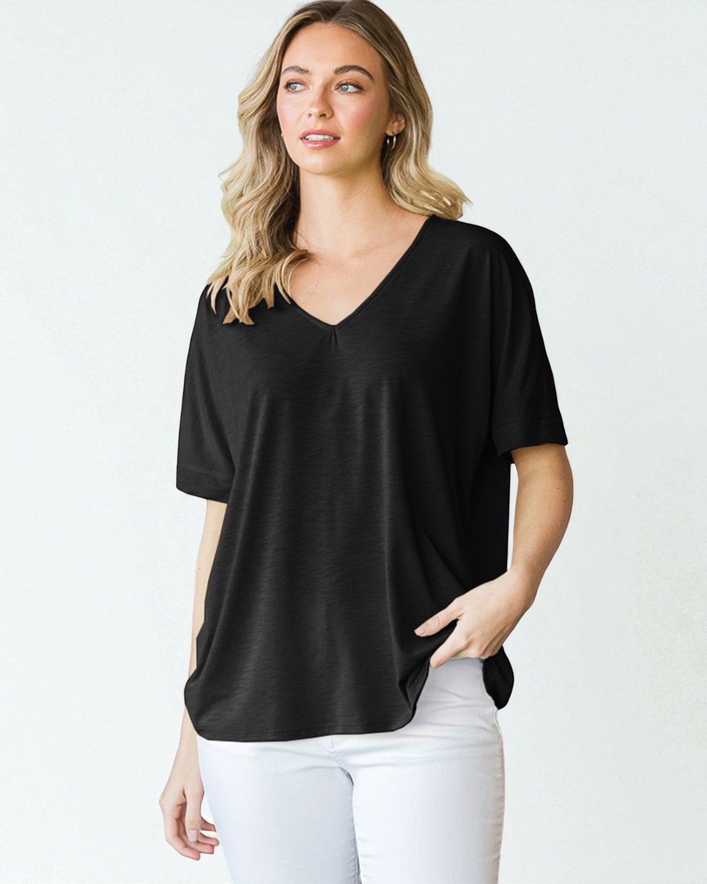 Woman wearing a black V-neck t-shirt and white pants on a plain background