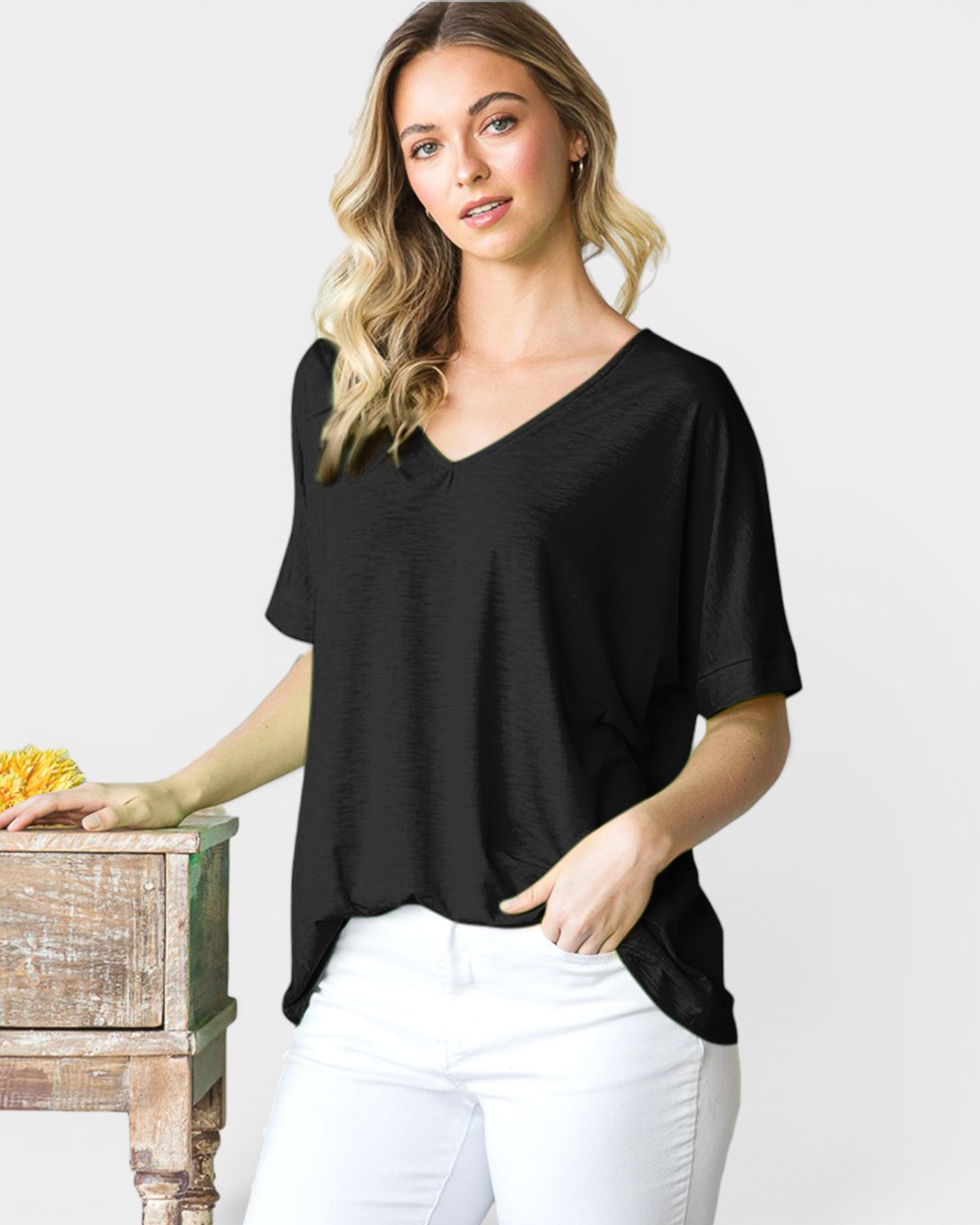 Woman wearing a black top and white pants against a plain background