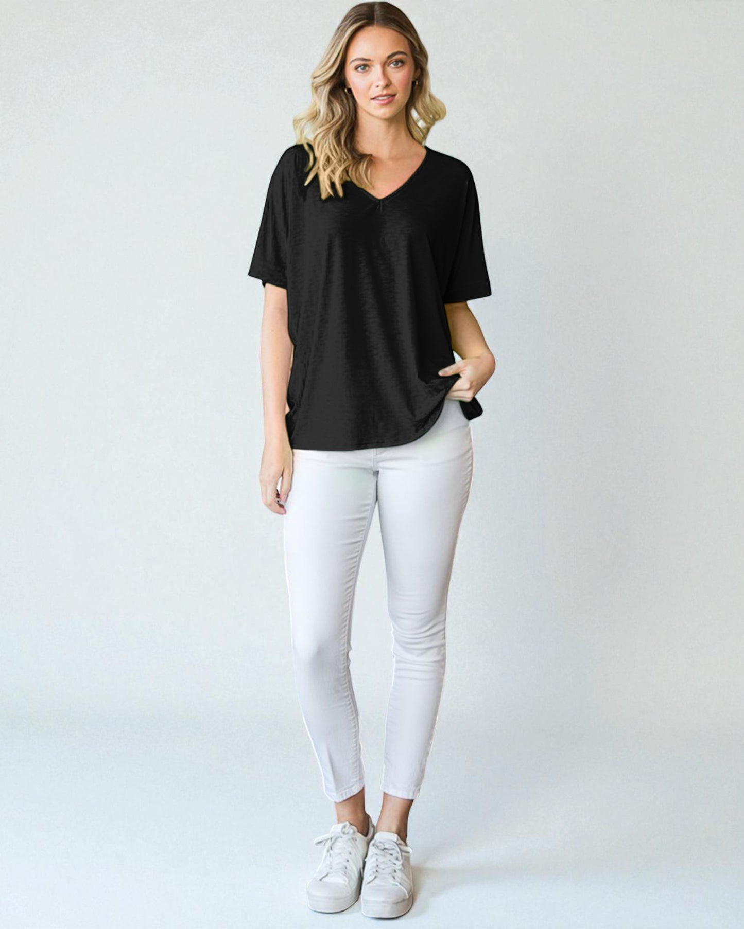 Woman wearing a black t-shirt and white pants on a plain background