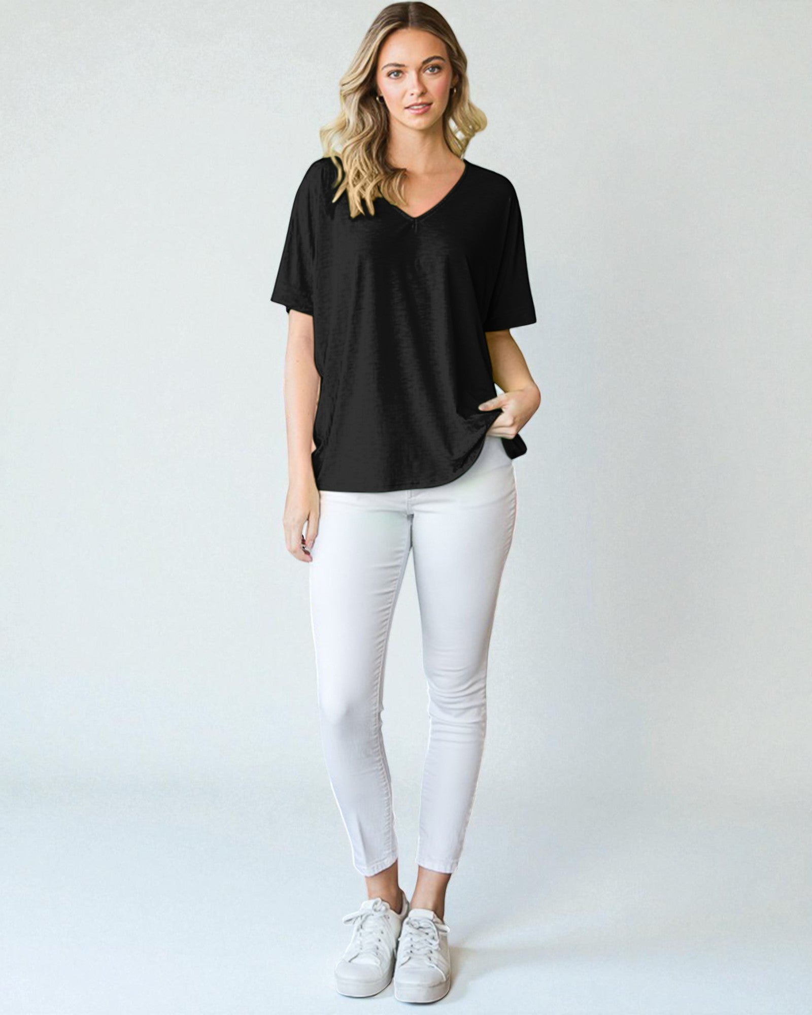 Woman wearing a black t-shirt and white pants on a plain background