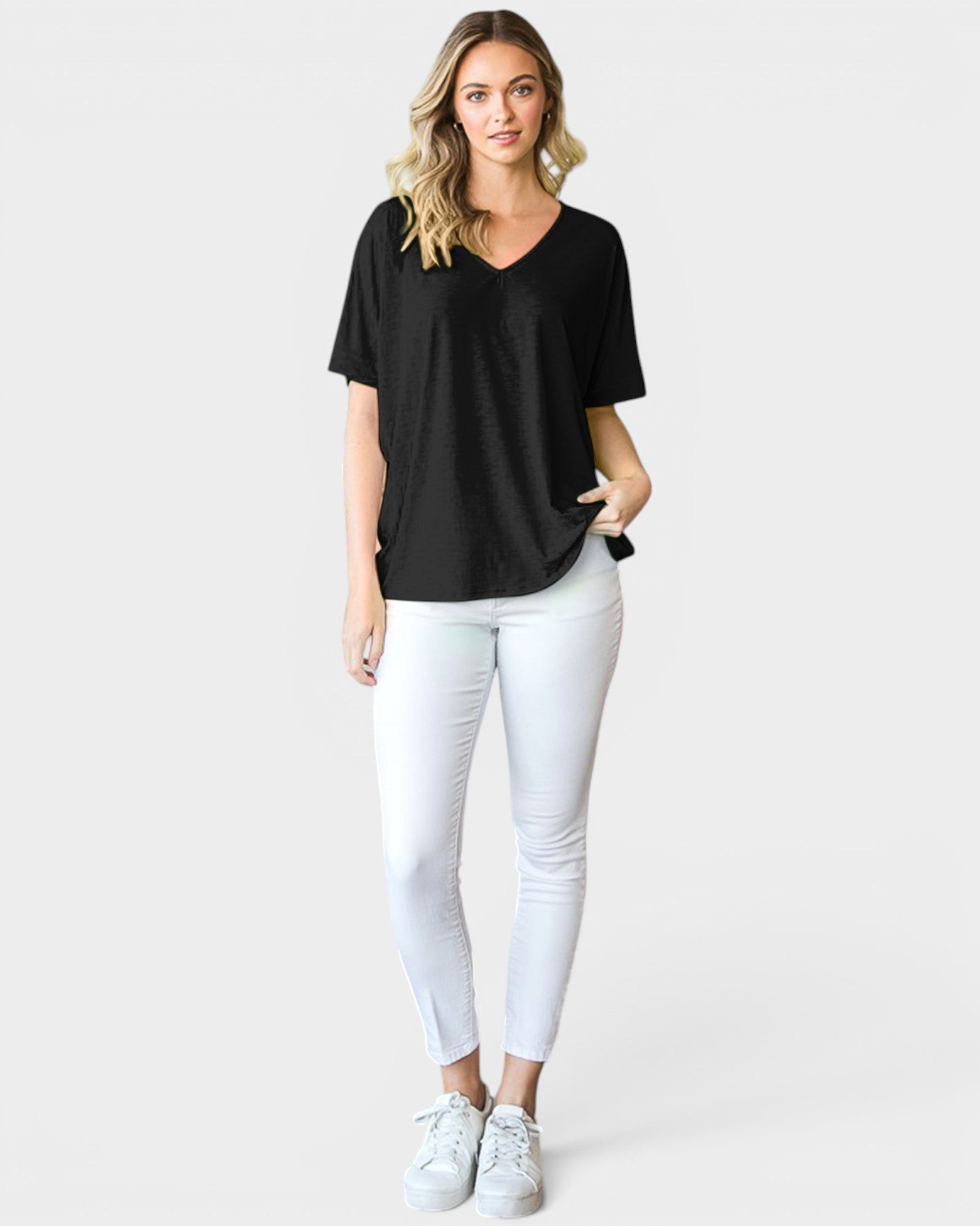Woman wearing a black t-shirt and white pants on a plain background