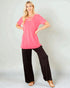 Woman wearing a pink top and black pants on a plain background
