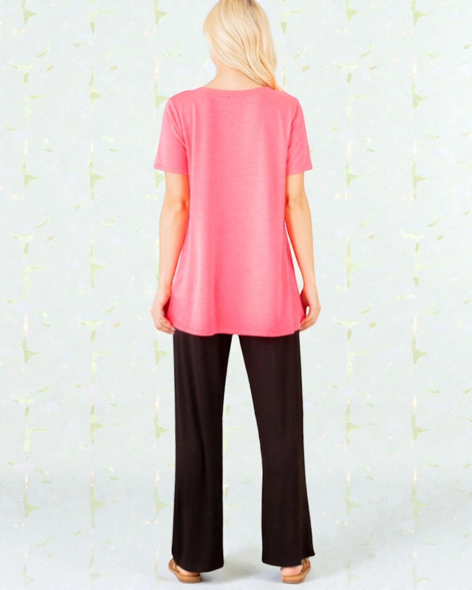 Person wearing a pink top and black pants against a light background