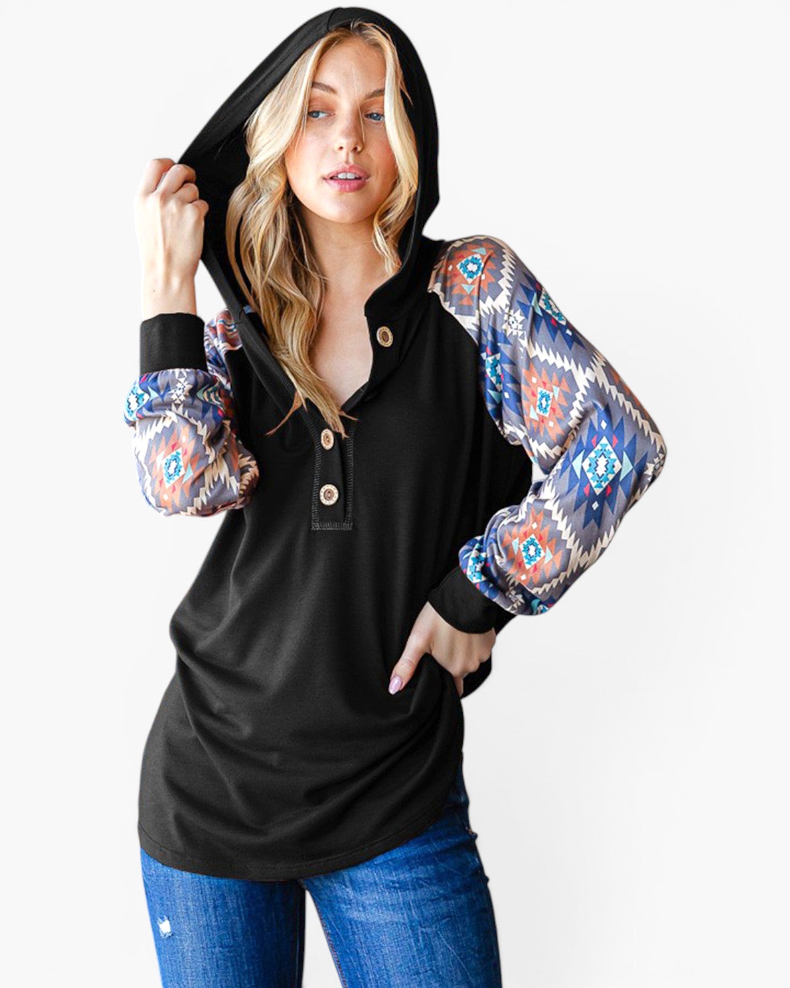 A woman modeling a black hooded long-sleeve top with patterned sleeves featuring a blue, orange, and white geometric Southwestern design, paired with blue jeans against a light gray background.