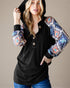 Woman wearing a black hoodie with colorful patterned sleeves against a neutral background