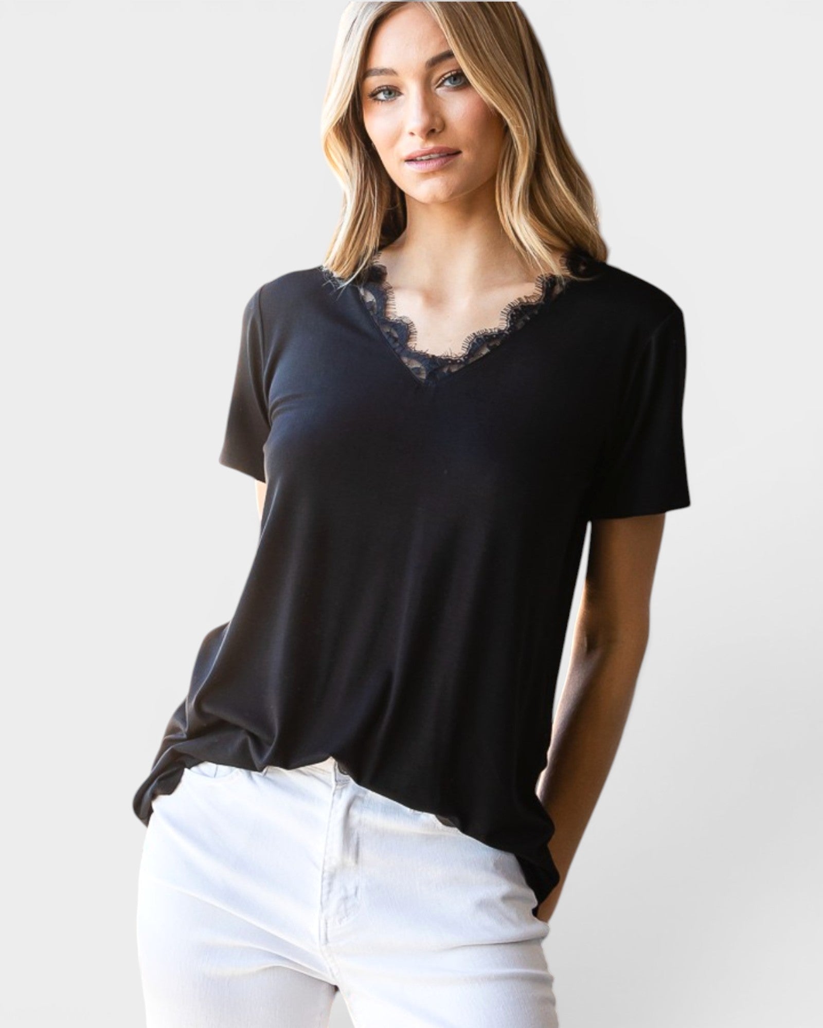 Woman wearing a black top with lace neckline and white pants on a plain background