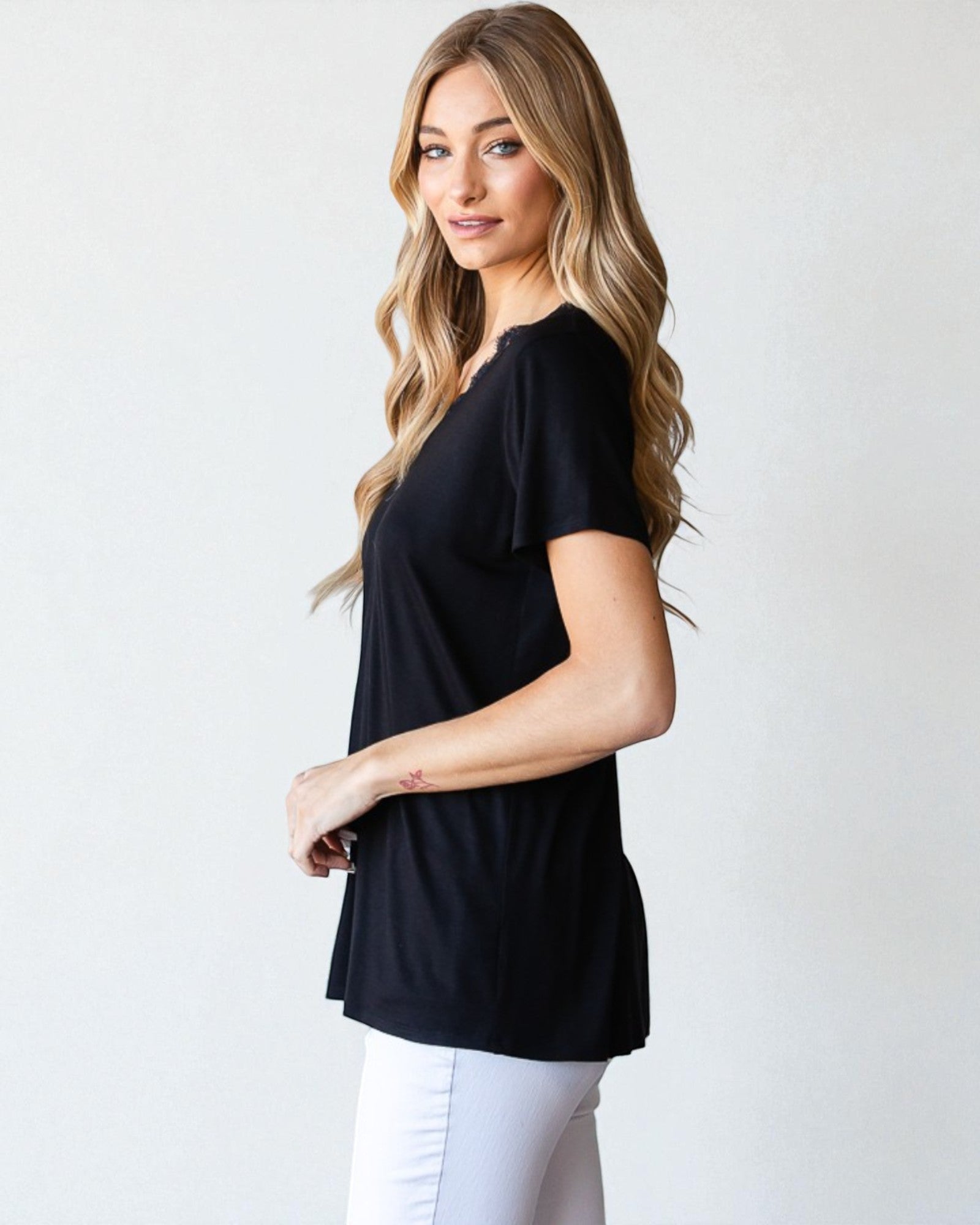 Woman wearing a black top and white pants against a plain background