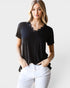 Woman wearing a black t-shirt with lace trim and white pants on a light gray background