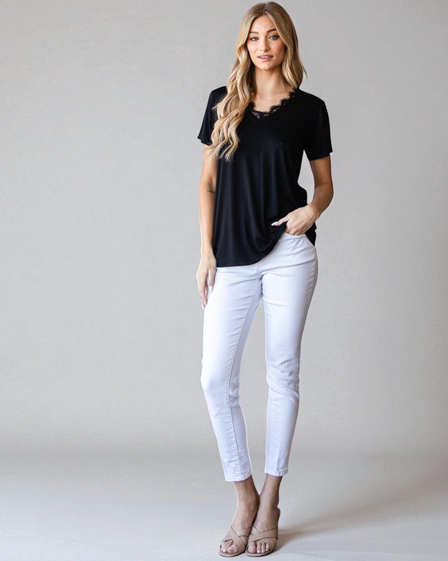 Woman wearing a black top and white pants against a plain background