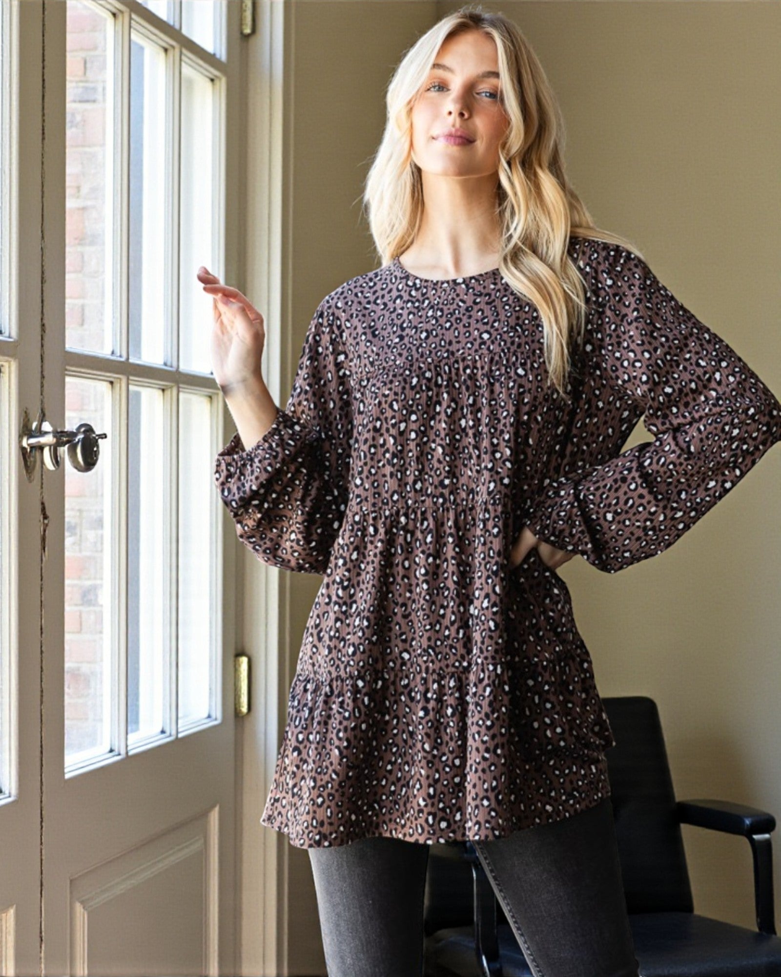 Woman wearing a patterned dress standing by a window indoors.