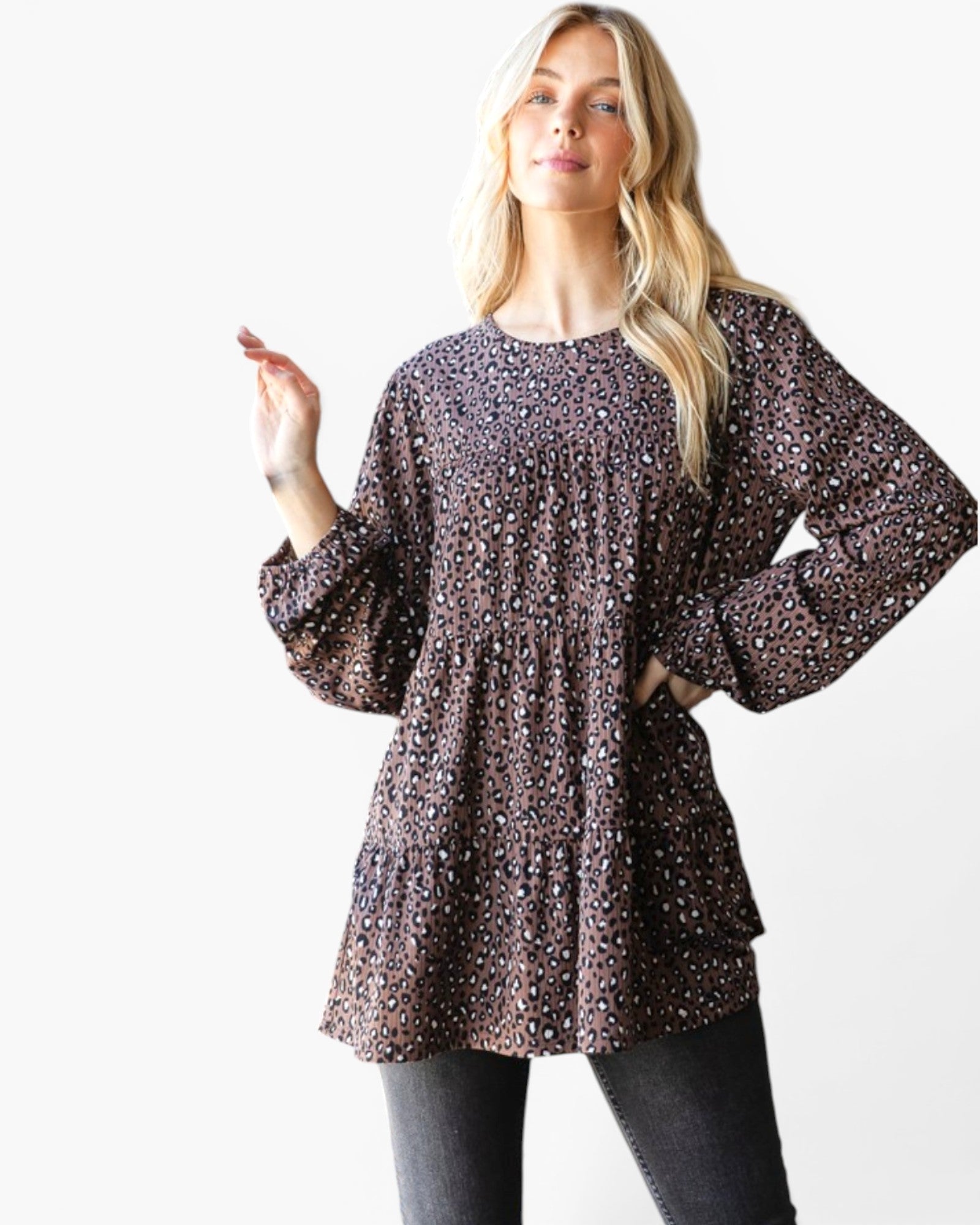 A woman modeling a long-sleeve tiered tunic top with a dark brown and black leopard print pattern, paired with dark gray jeans, against a plain white background.
