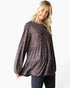 A woman modeling a long-sleeve peplum top with a dark brown and black leopard print pattern, paired with dark jeans, against a plain white background.