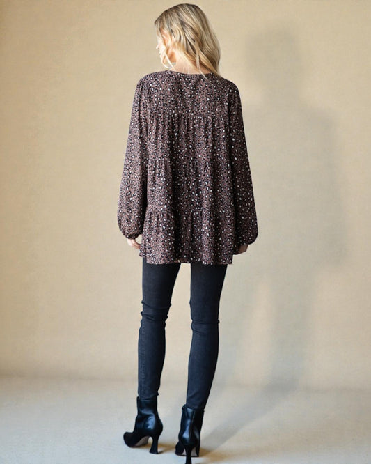 Person wearing a long-sleeve patterned top and dark jeans against a plain background