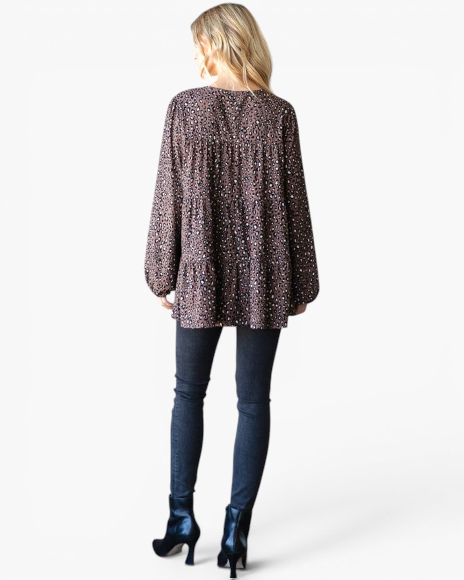 A woman shown from the back wearing a loose, long-sleeve top with a dark brown and black speckled pattern, paired with dark blue skinny jeans and dark blue high-heeled boots, against a light gray studio background.