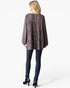 A woman shown from the back wearing a loose, long-sleeve top with a dark brown and black speckled pattern, paired with dark blue skinny jeans and dark blue high-heeled boots, against a light gray studio background.