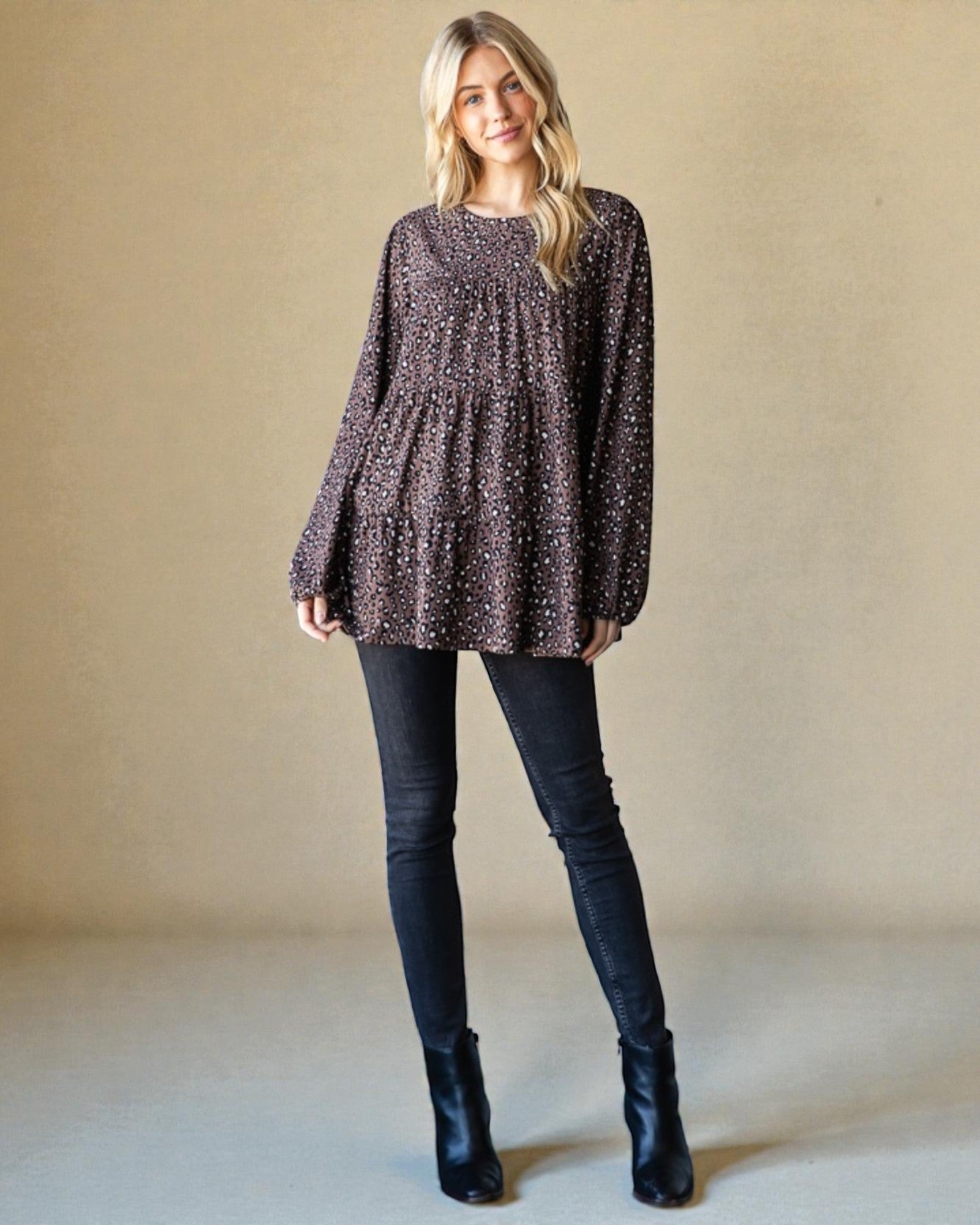 Woman wearing a patterned long-sleeve top and black pants against a beige background