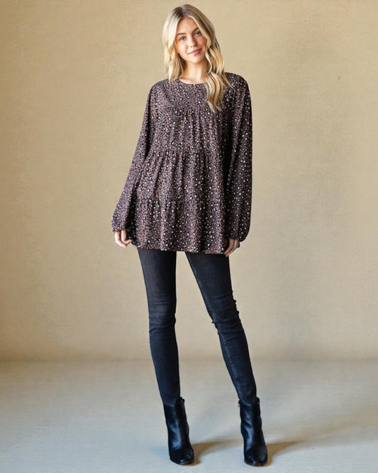 Woman wearing a patterned long-sleeve top and black pants against a beige background