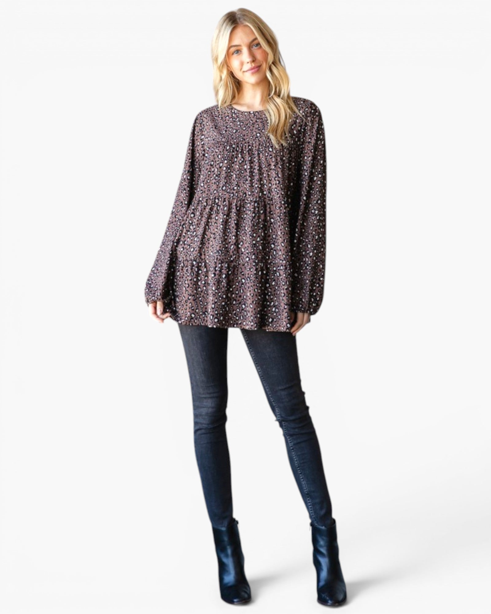 A woman modeling a long-sleeve, gathered peplum-style top with a dark brown and black speckled pattern, paired with dark blue skinny jeans and metallic blue ankle boots, against a plain white studio background.