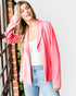Woman wearing a pink cardigan over a white top and blue jeans, standing against a light gray background.