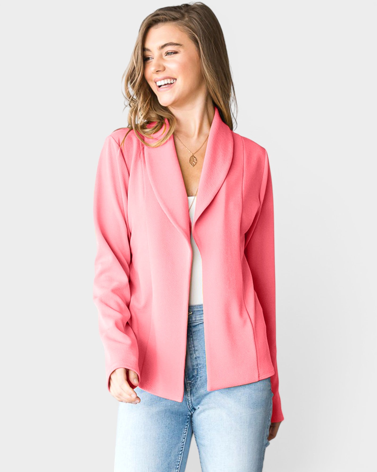 Woman wearing a pink blazer over a white top and blue jeans on a light gray background