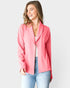Woman wearing a pink blazer over a white top and blue jeans on a light gray background