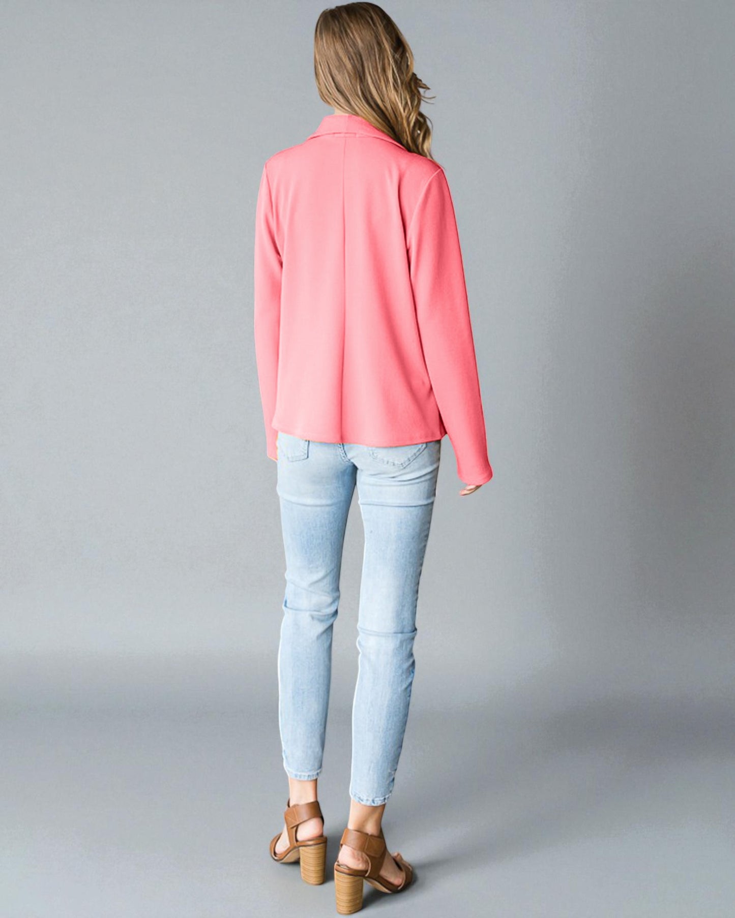 Woman wearing a pink blazer and light blue jeans on a gray background