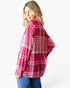 A woman wearing an oversized pink and white plaid flannel shirt, shown from a three-quarters back view against a plain white background.