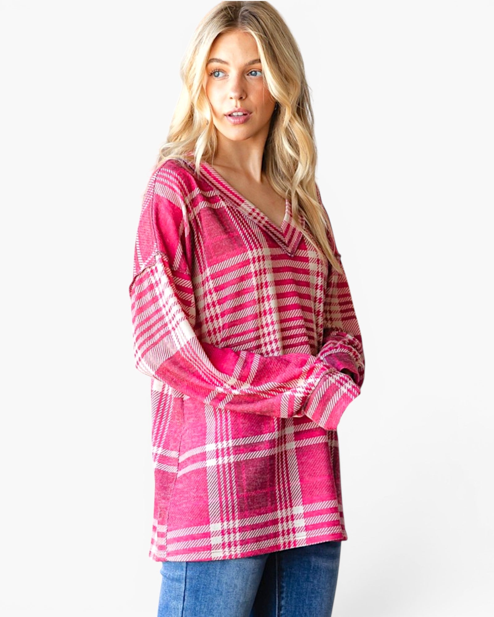 A woman modeling a pink and white plaid long-sleeve top with a V-neck, paired with blue jeans, against a plain white studio background.