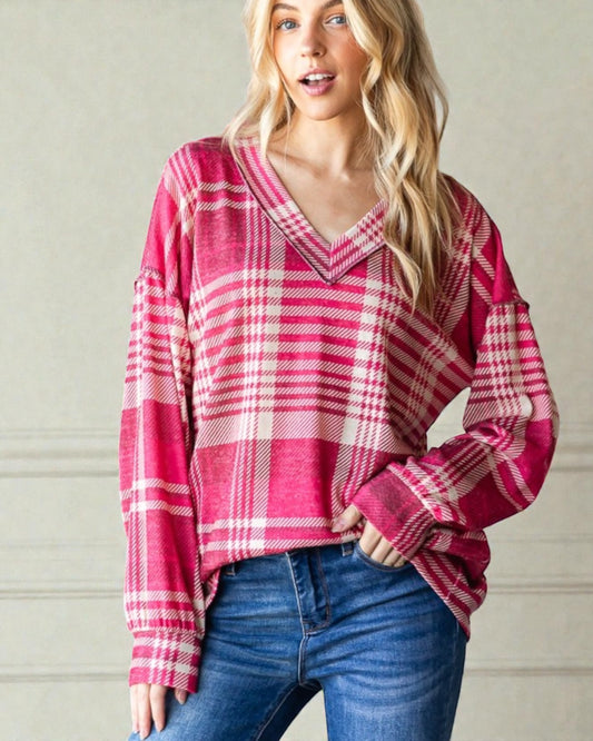 Woman wearing a pink plaid sweater and blue jeans against a neutral background