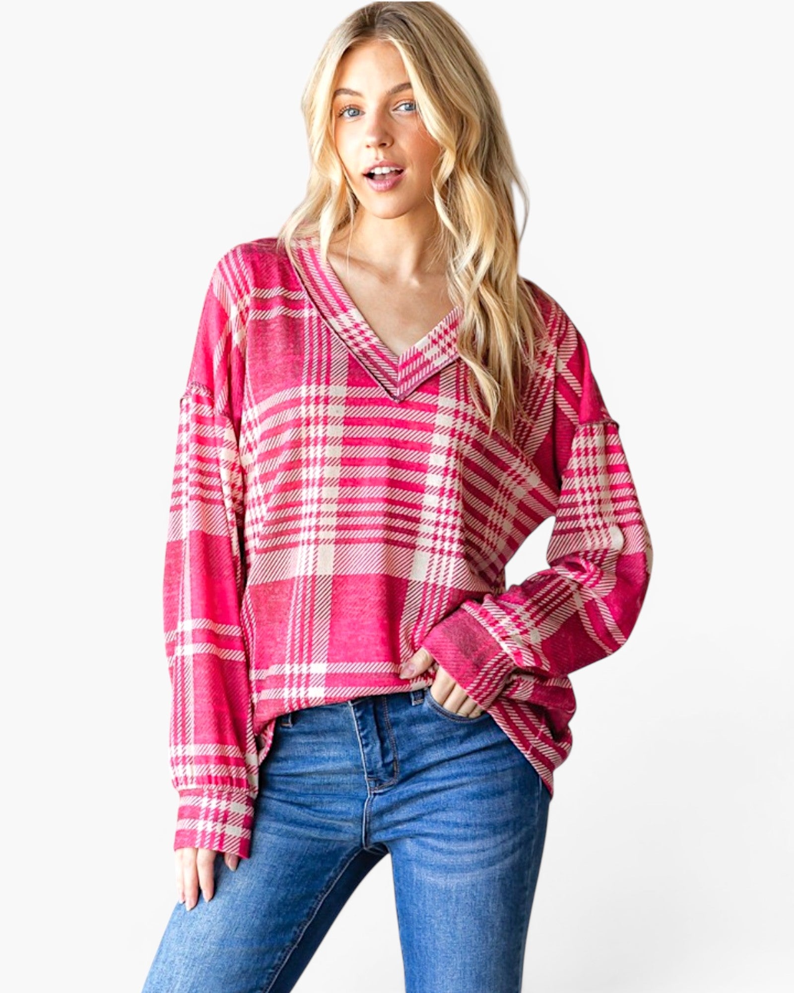 A woman modeling a pink and white plaid long-sleeve knit top with a V-neck, paired with blue jeans, against a plain white studio background.