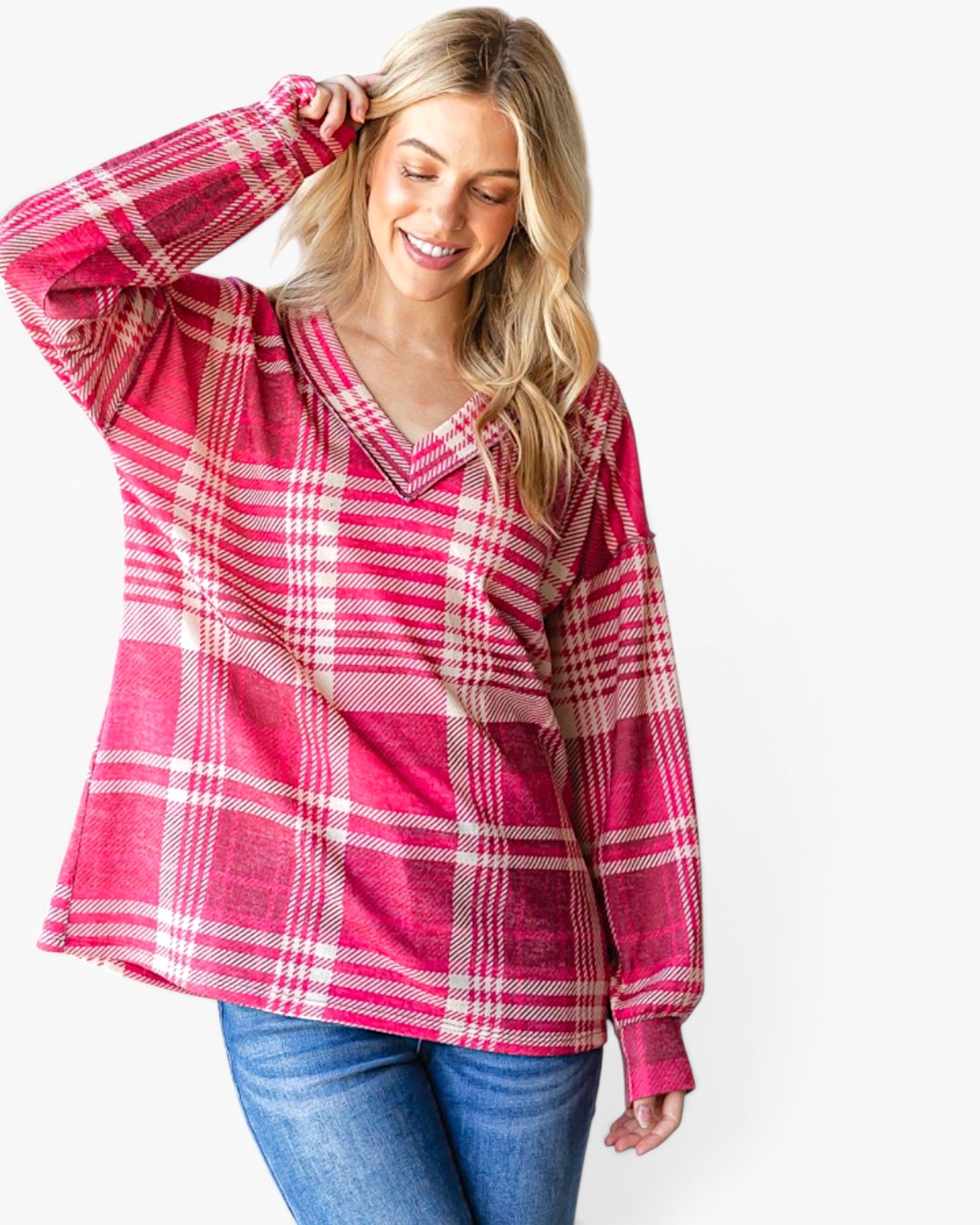 A woman wearing a pink and white plaid long-sleeve top with blue jeans, posing against a light gray background.