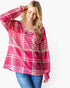A woman wearing a pink and white plaid long-sleeve top with blue jeans, posing against a light gray background.