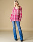 Woman wearing a pink plaid shirt and blue jeans against a beige background