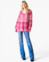 A woman modeling a pink and white plaid long-sleeve collared shirt with blue flare jeans against a plain white studio background.