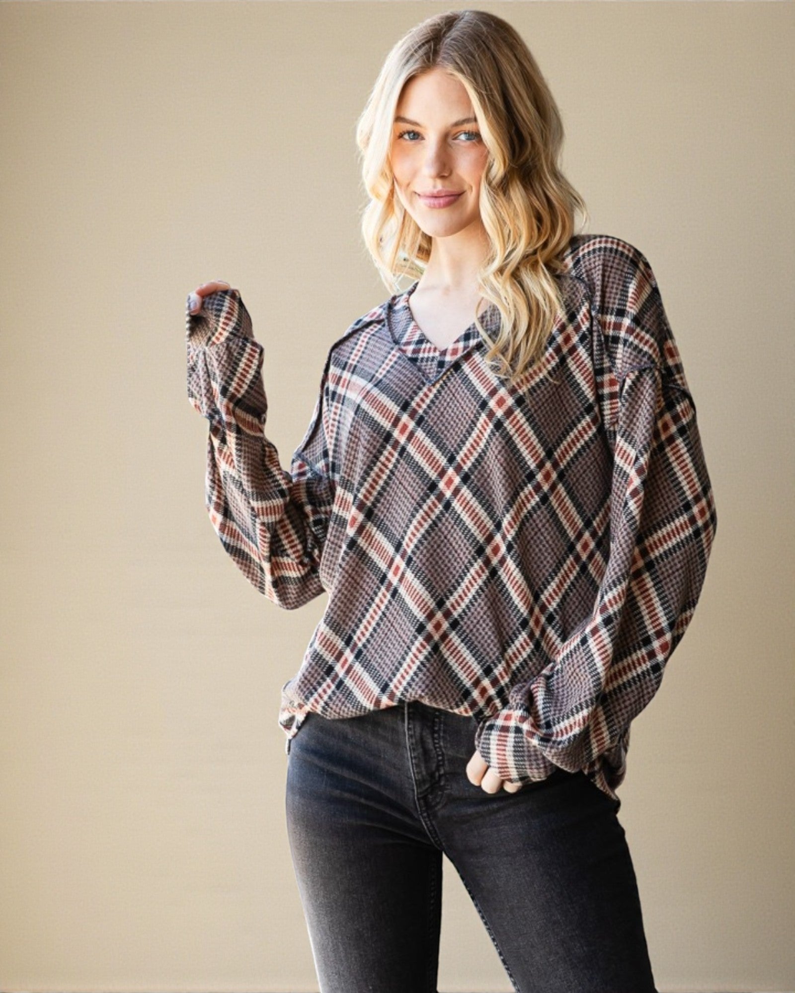 Woman wearing a plaid shirt and dark jeans against a beige background