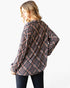 A woman wearing an oversized long-sleeve plaid button-up shirt in black, white, and red, shown from a three-quarters back view against a plain white background.