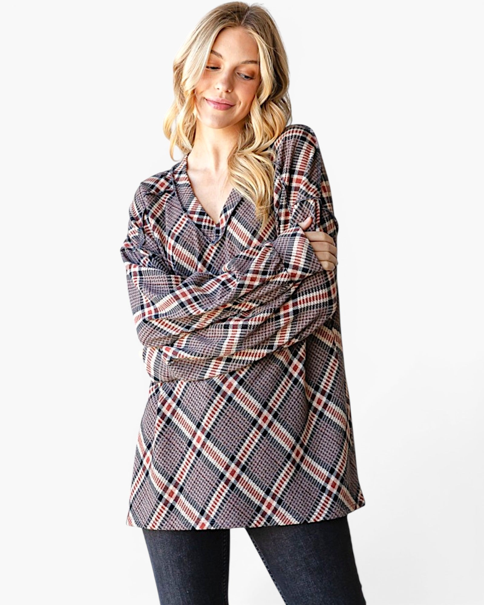 A woman modeling a long-sleeve plaid tunic top with a black, white, and red pattern, paired with dark jeans, against a plain white background.
