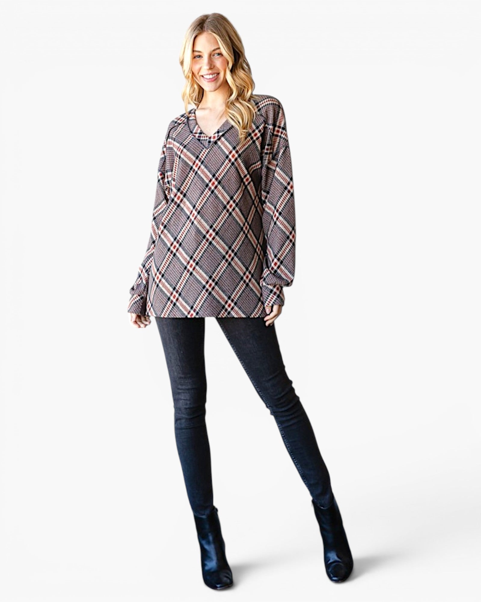 A woman modeling a long-sleeve plaid blouse with dark skinny jeans and dark blue ankle boots, standing against a plain white studio background.