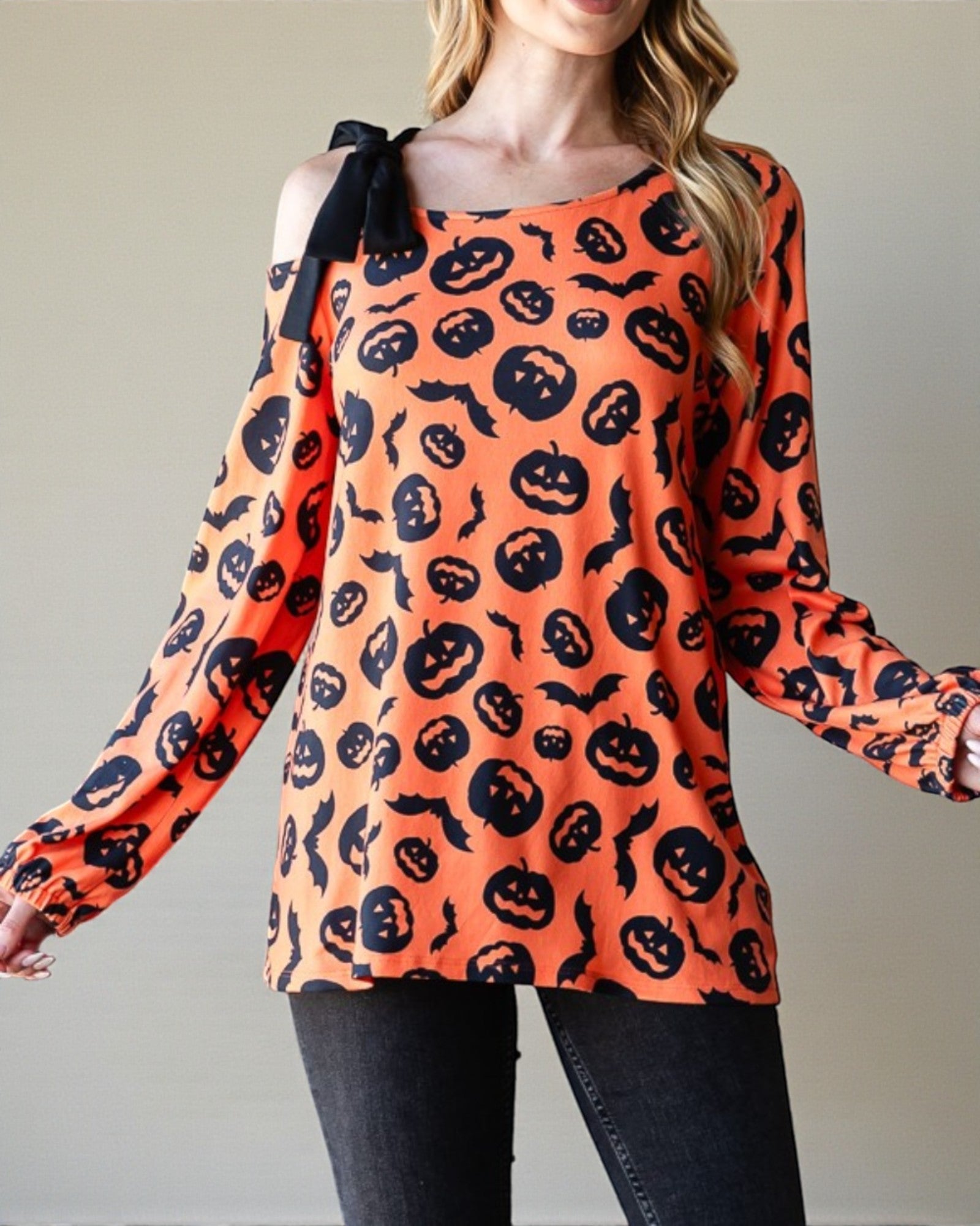 Person wearing an orange long-sleeve top with black pumpkin pattern against a neutral background